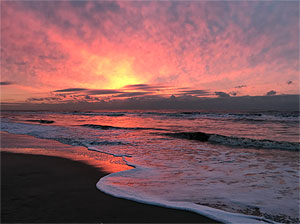 Sonnenuntergang an einem Strand. Gischt fließt von rechts über den feuchten Sand.